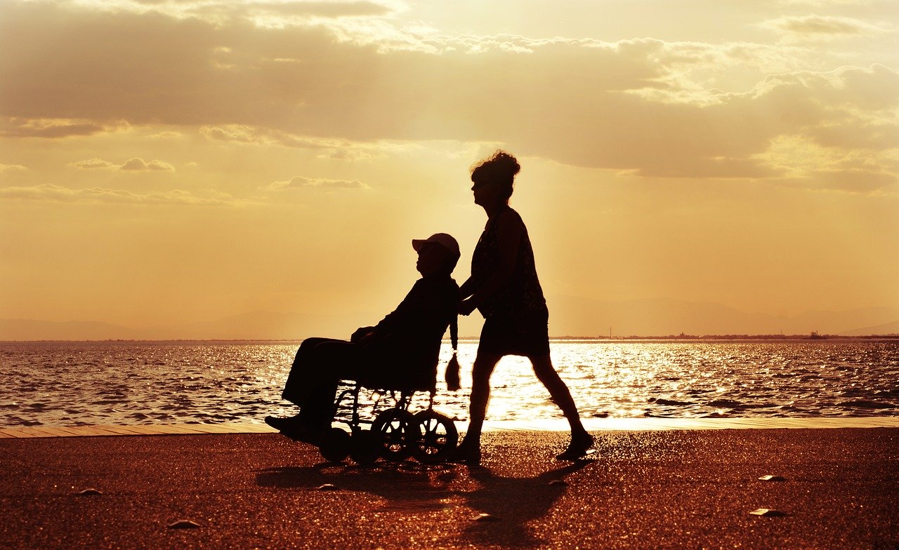 Assistent med kund i rullstol i solnedgång. Foto: Pixabay